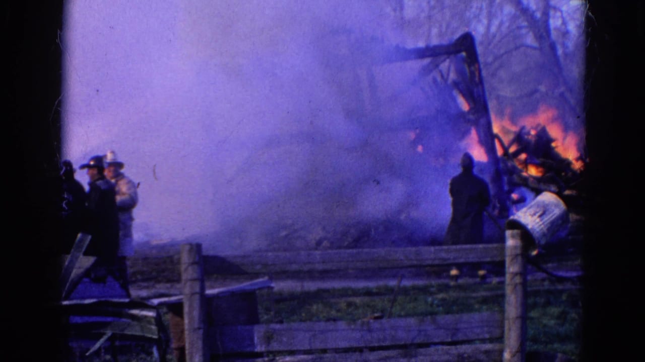 1968 Wauconda, Illinois 8mm frame showing firefighters near a wooden fence while a structure burns behind thick smoke.