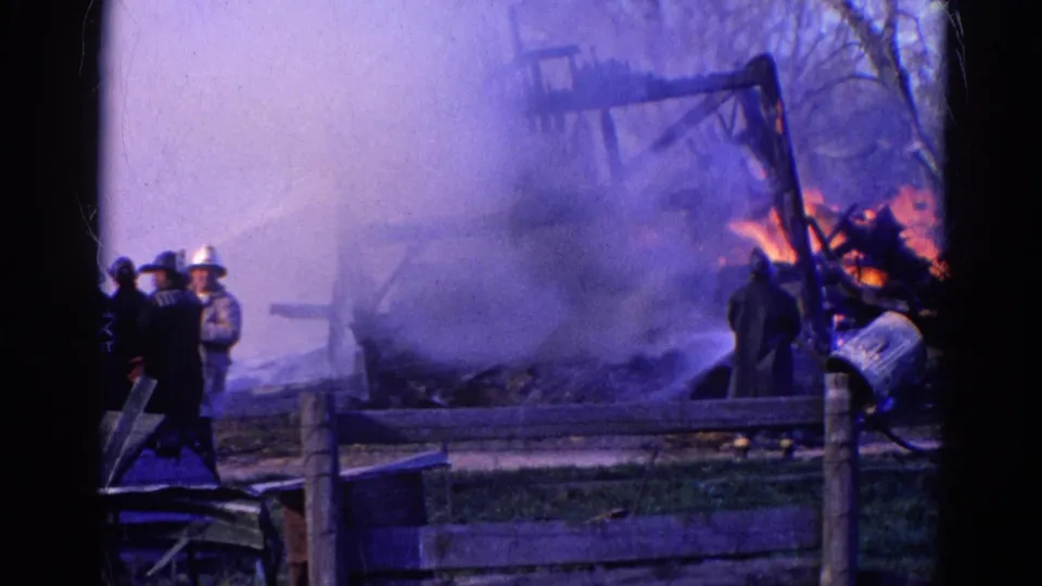 1968 Wauconda, Illinois frame with firefighters beside a smoky structure fire and visible flames at the right edge.