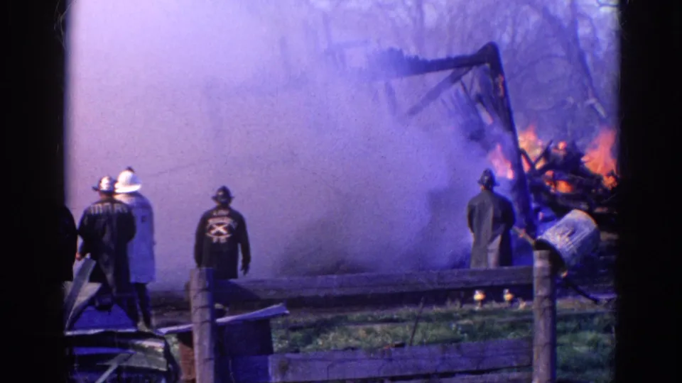 1968 Wauconda, Illinois 8mm frame showing helmeted firefighters by a fence as dense smoke covers the burning structure.