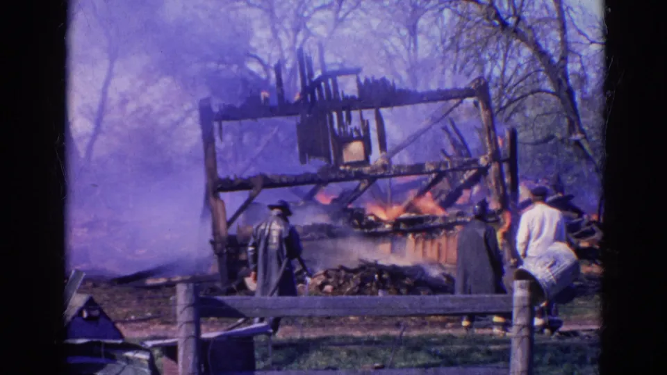 Wauconda, Illinois barn fire scene with smoke, visible flames, responders, and a wooden fence in a 1968 8mm home-movie frame.