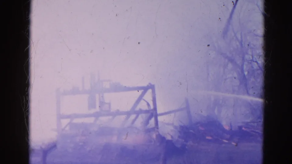 The final 1968 Wauconda frame is heavily obscured by smoke, with a collapsed wooden frame and low flames still visible in the debris.