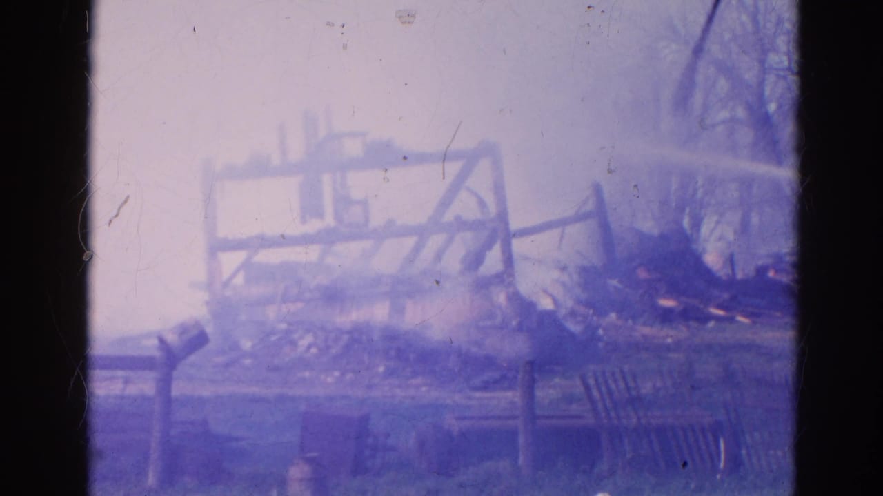Charred structure and debris seen through a purple-blue 8mm film frame.