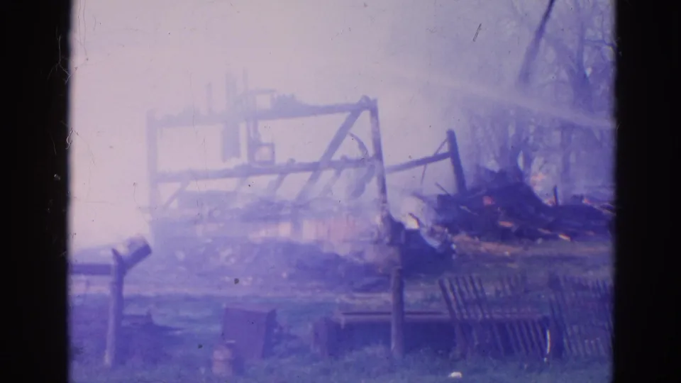 1968 Wauconda, Illinois 8mm footage frame with a scorched structure, twisted debris, fence posts, and bluish film fading.