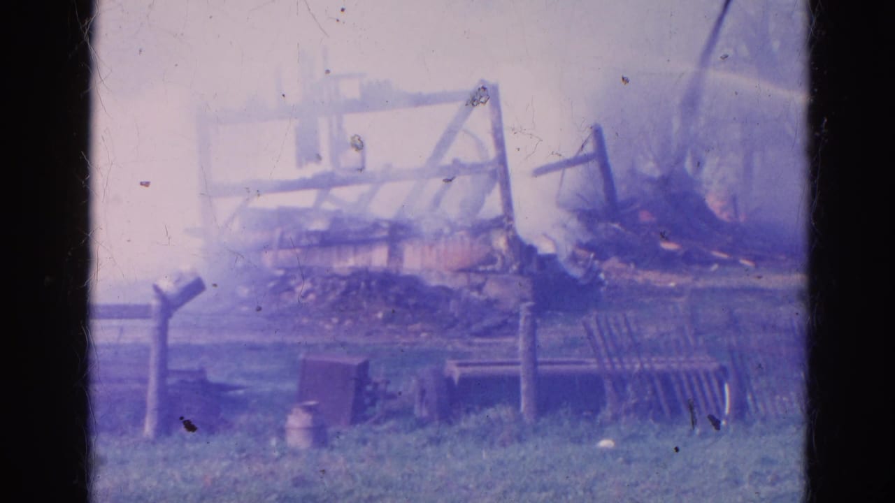 1968 Wauconda 8mm frame showing a burned rural structure, smoke, scattered debris, fencing, and grassy foreground.