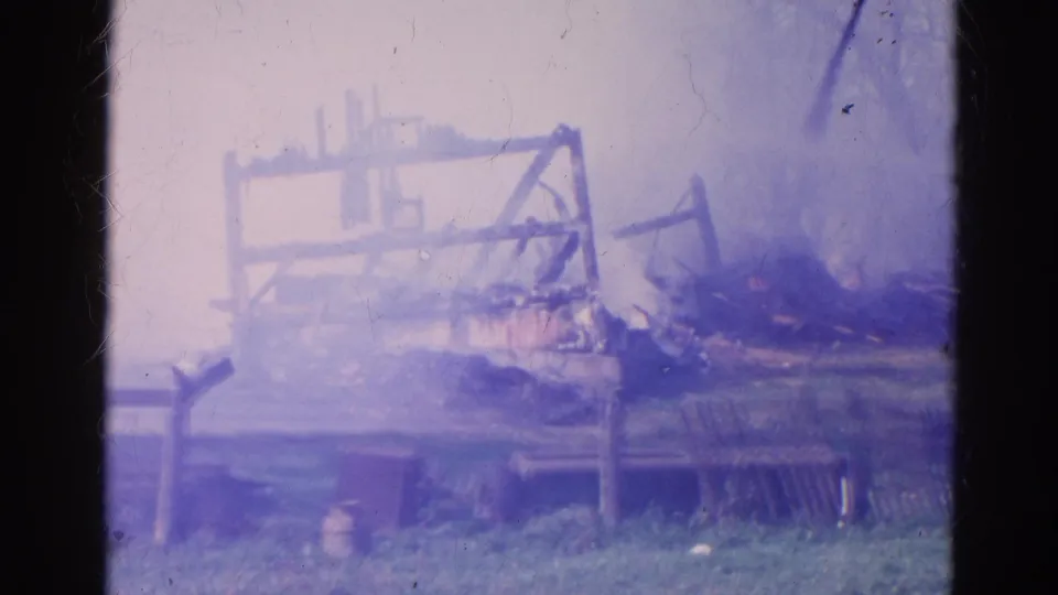 Soft 8mm frame from 1968 Wauconda showing smoke over a burned farm structure with fencing and debris in view.