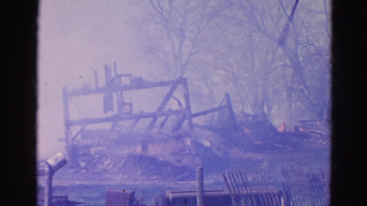 1968 Wauconda 8mm frame showing a burned wooden structure smoking among bare trees and debris.