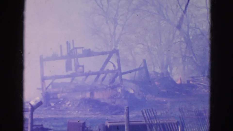 1968 Wauconda 8mm frame showing a burned wooden structure smoking among bare trees and debris.