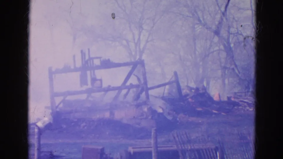 1968 Wauconda frame with smoke drifting across charred beams, collapsed debris, and leafless trees.