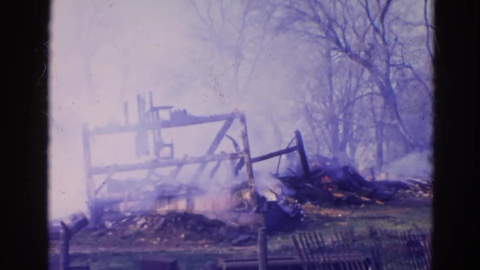 1968 Wauconda frame showing the burned structure further obscured by smoke, rubble, and leafless trees.