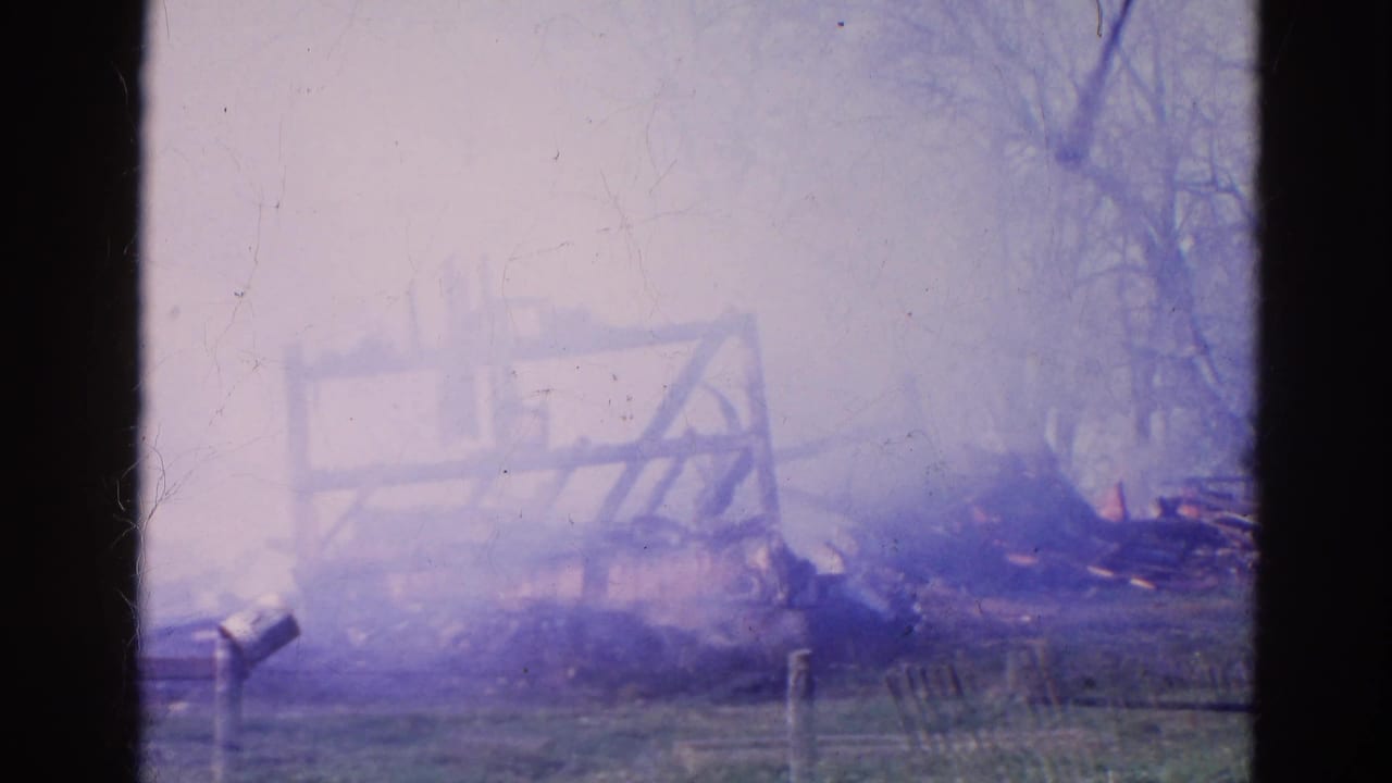 Smoke rising around a partially burned barn seen through a dark window frame.