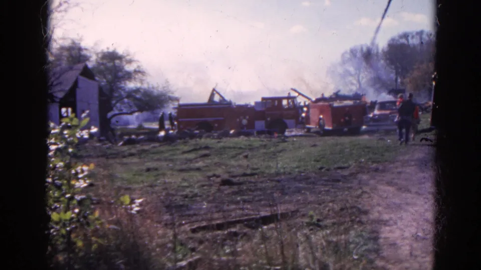 Red fire trucks, smoke, onlookers, and a parked vehicle are seen from a handheld 8mm viewpoint in Wauconda, Illinois, in 1968.