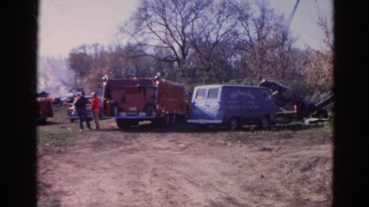 1968 Wauconda, Illinois home-movie frame showing emergency vehicles and people near a rural destruction scene.