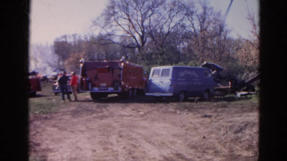 1968 Wauconda, Illinois home-movie frame showing emergency vehicles and people near a rural destruction scene.