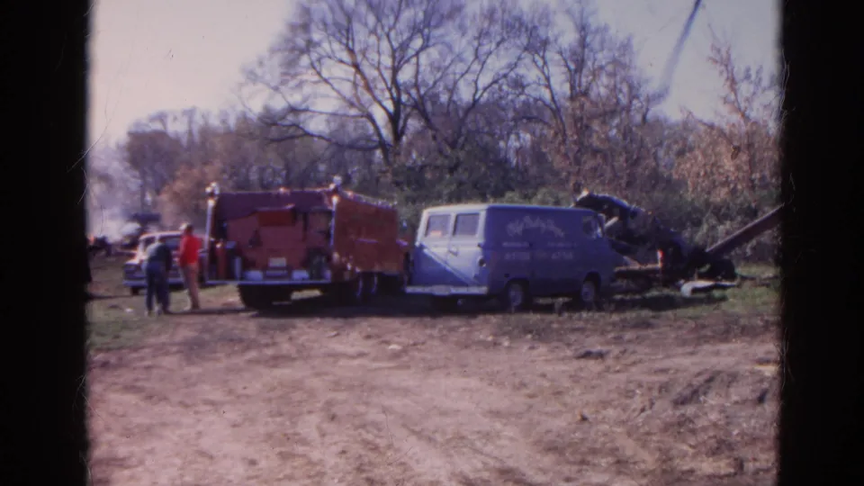 1968 Wauconda frame with a red fire truck, blue service van, responders, and haze near a rural debris area.