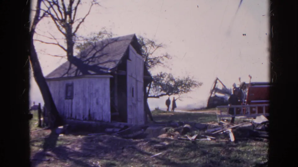 1968 Wauconda frame of a rural damaged area with shed, debris, responders, and fire apparatus in bright daylight.