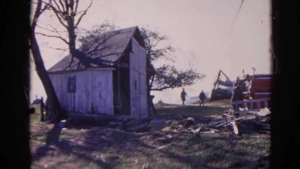 1968 Wauconda, Illinois 8mm frame showing a shed, bare trees, scattered wood, and two people walking across the background.