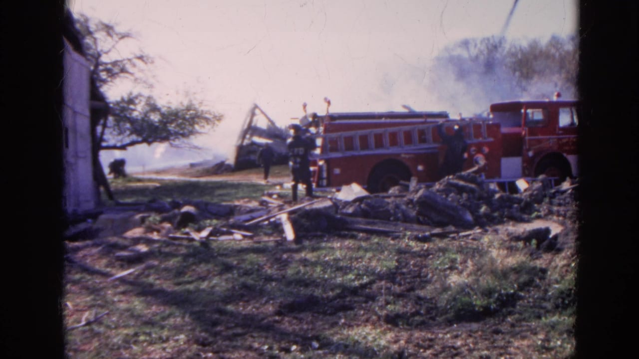 Firefighters and a red fire truck near smoking debris from a structure fire.