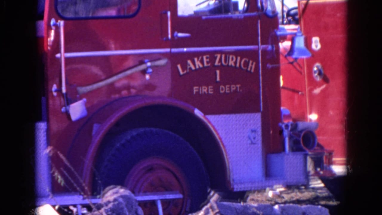 1968 home-movie frame of the Lake Zurich Fire Dept. truck, showing the side lettering, open cab area, large wheel, bell, and front hose hardware.
