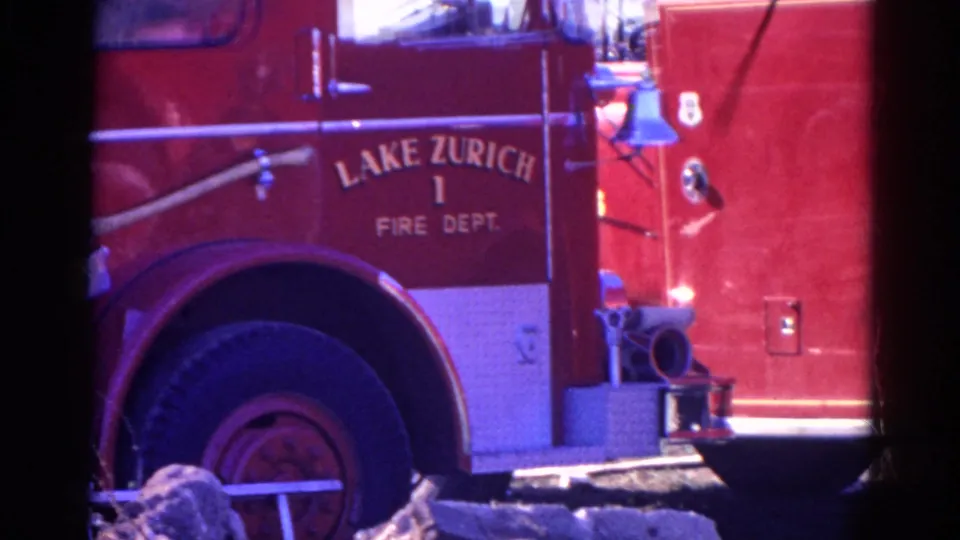 1968 8mm frame showing a close side view of the red Lake Zurich Fire Dept. truck with wheel, side panel, white trim, hose fitting, and heavy film borders.