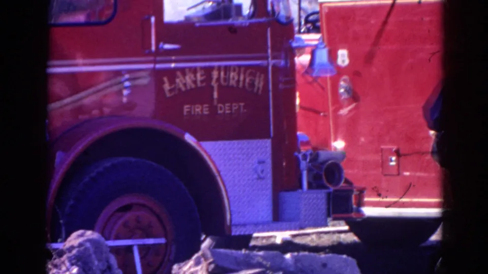 1968 Wauconda-area frame of the Lake Zurich Fire Dept. truck side, with painted lettering, front wheel, bell, hose fitting, and a partial figure at the right edge.