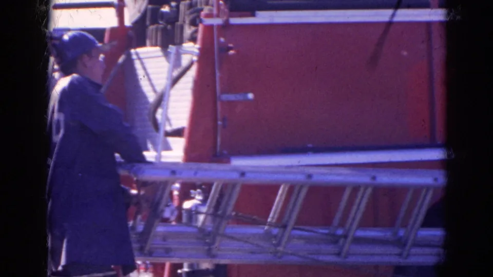 A firefighter in a dark coat stands beside the red fire truck, with mounted ladders and equipment visible in the 1968 scene.