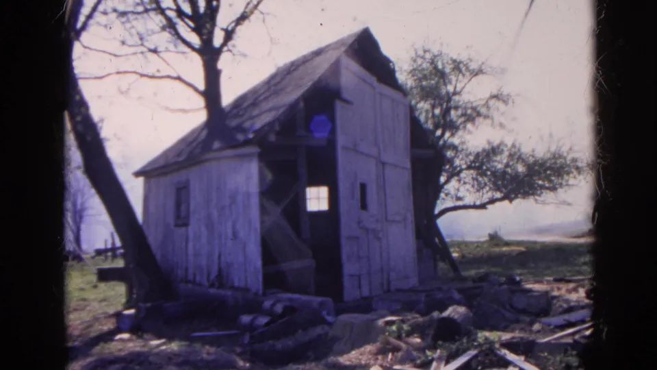 A weathered wooden shed in rural Wauconda, Illinois appears among bare trees, grass, and scattered debris in 1968 home-movie footage.
