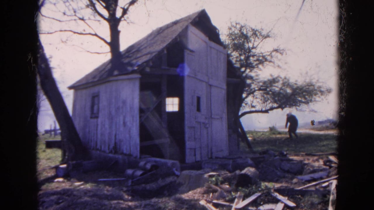1968 Wauconda, Illinois 8mm frame showing a weathered white shack, bare trees, scattered debris, and a distant man bending near the field.