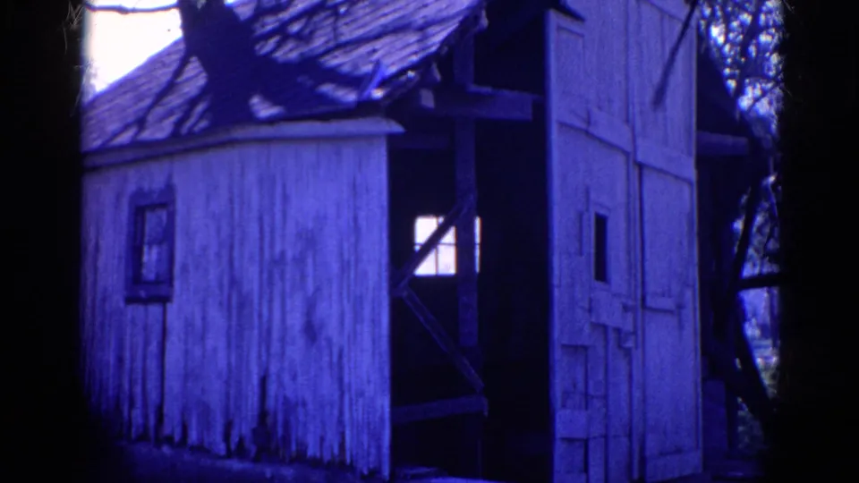 Closer 1968 Wauconda 8mm view of the weathered white shack, open door, small window, tree shadows, and dark interior framing.