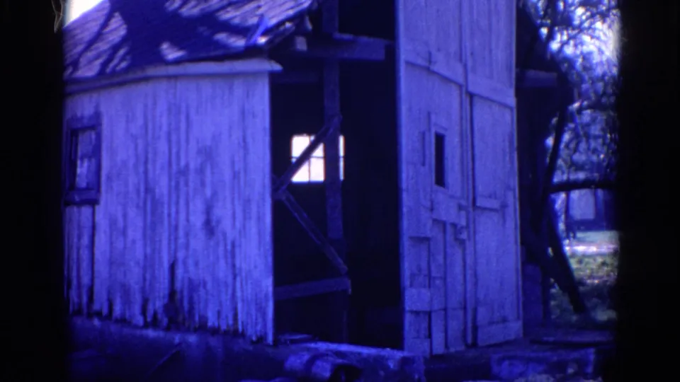 1968 Wauconda 8mm frame showing a weathered white wooden shack partly obscured by dark trees and blue color shift.