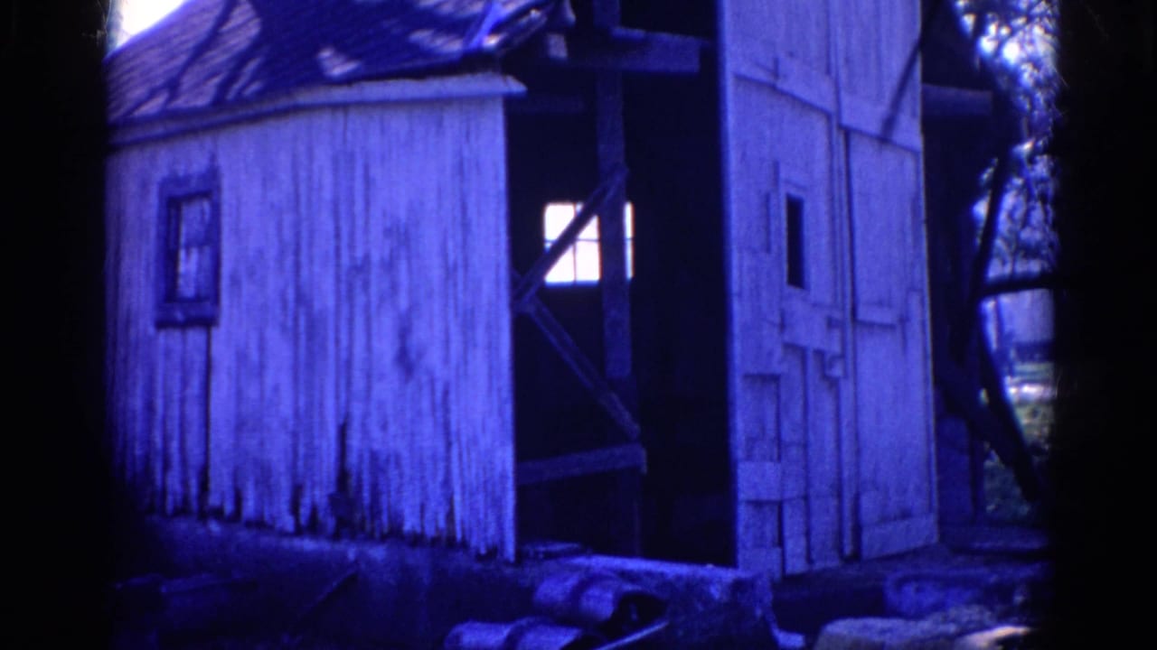 1968 Wauconda frame with a weathered white shack, small window, open side structure, tree trunks, and blue-tinted yard light.
