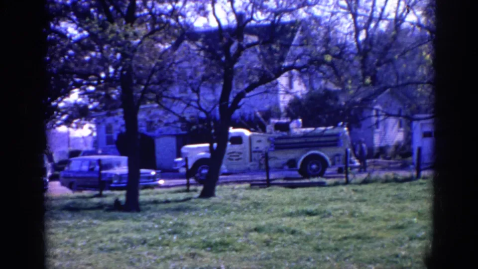 A blue-cast 8mm view of a white fire truck and parked cars near houses in Wauconda, Illinois, with trees framing the scene.