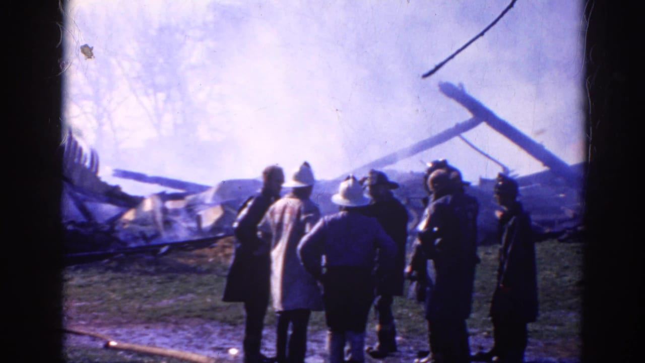 Firefighters and bystanders stand near a smoking collapsed structure.