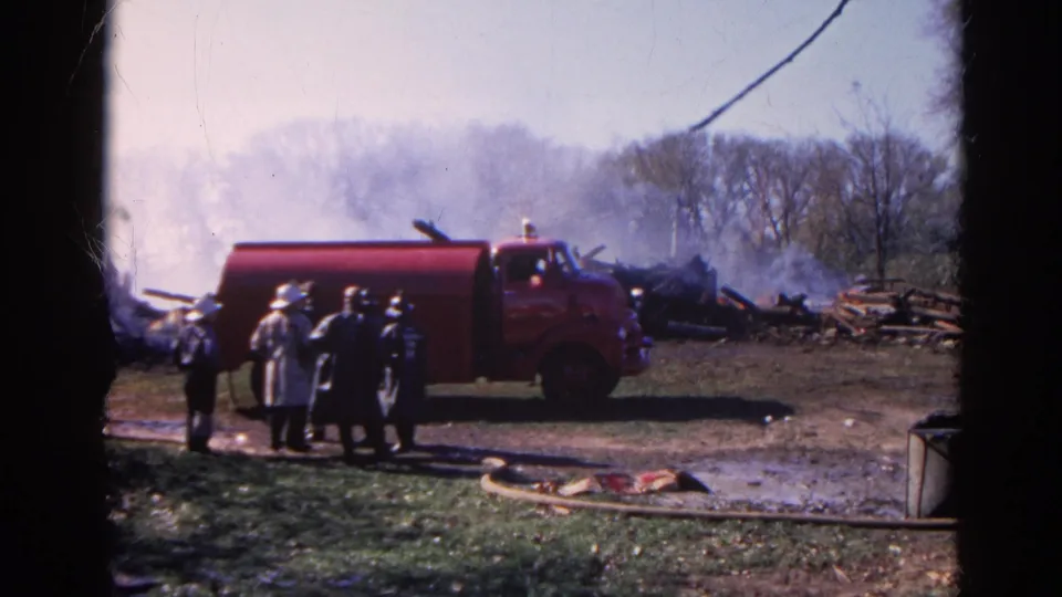1968 Wauconda 8mm frame showing firefighters standing by a red fire truck, with smoke and debris in the background.