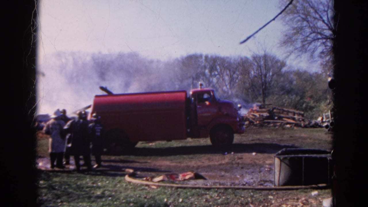 1968 Wauconda-area home-movie frame showing a red rural fire truck near firefighters, hose lines, smoke, and debris.