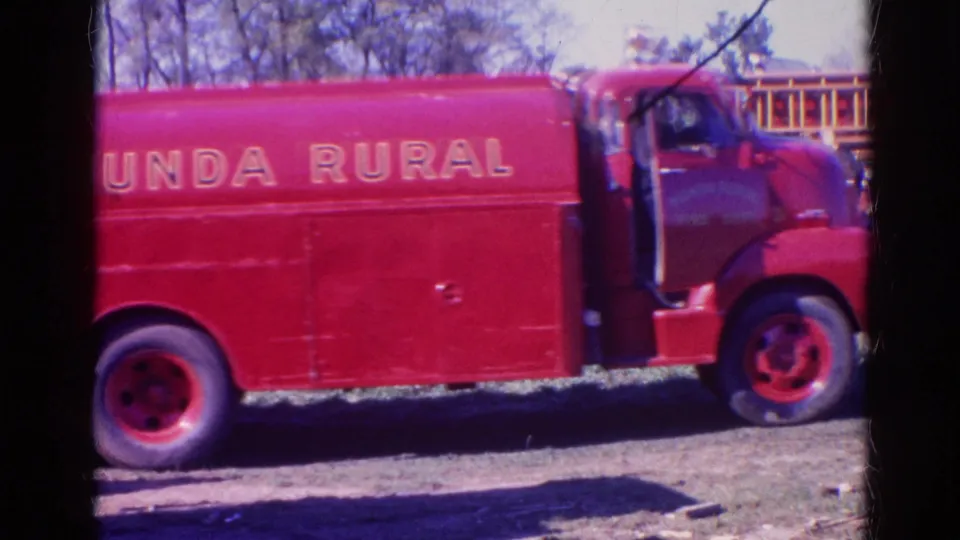 Close 8mm view of the red fire truck side with Nunda Rural lettering, wheel, cab, and a building partly visible behind it.