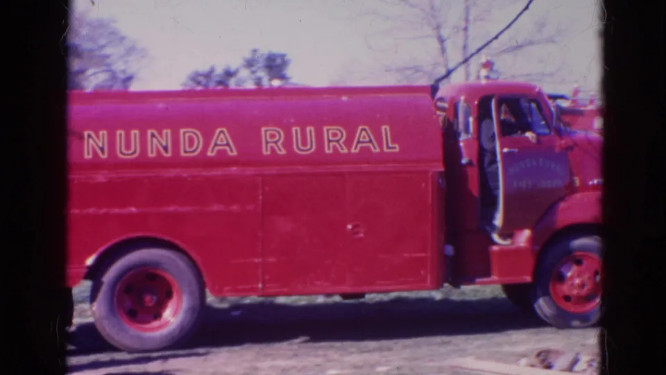 Close 1968 home-movie frame of the Nunda Rural fire truck side, showing lettering, red wheels, cab area, and dark gate border.