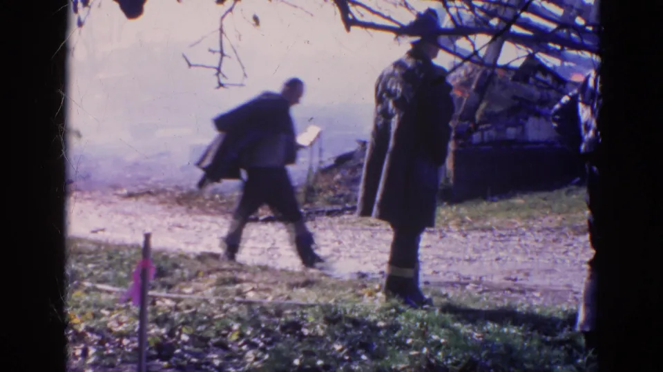 1968 Wauconda, Illinois 8mm frame showing one man crossing with a coat as another stands near a smoky rural fire scene.