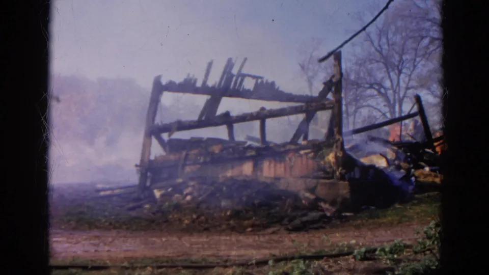 The 8mm frame shows a smoldering, burned wooden structure in Wauconda, Illinois, with debris and bare trees nearby.