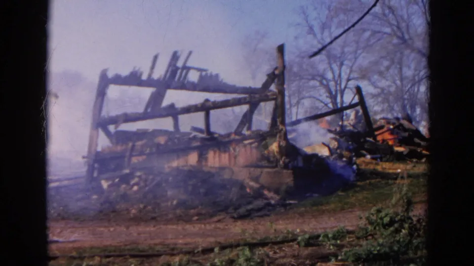 A smoky view of the burned structure in 1968 Wauconda shows charred beams, debris, grass, and bare trees.