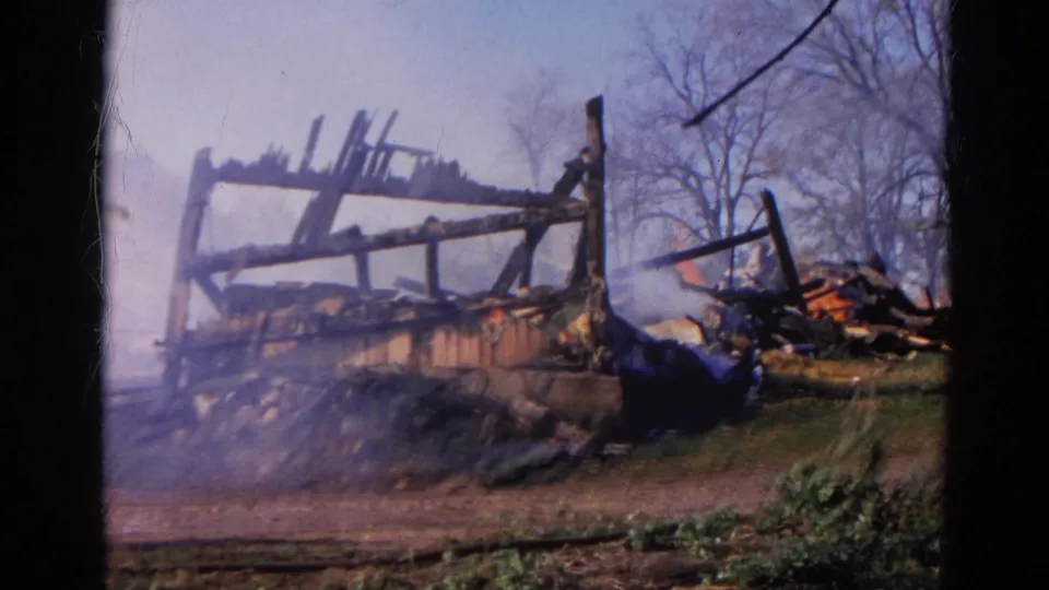 1968 Wauconda, Illinois 8mm frame showing a burned wooden structure with smoke, flame, rubble, and bare trees.
