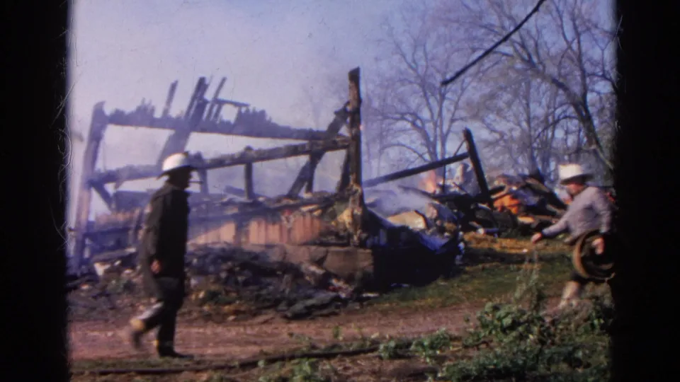1968 Wauconda, Illinois frame with firefighters approaching smoky rubble and charred beams at a structure fire.