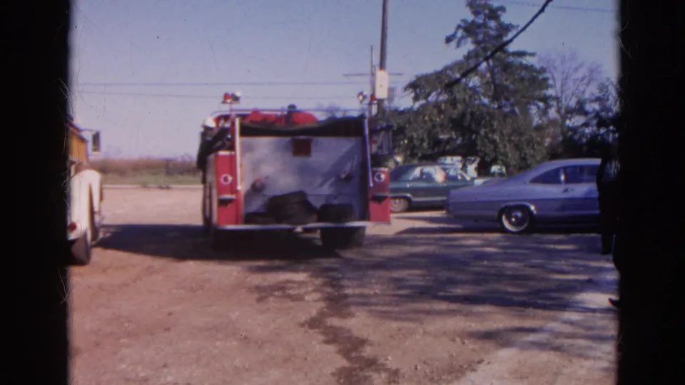 1968 Wauconda 8mm frame showing a red fire truck, parked late-1960s cars, utility pole, and open dirt lot.