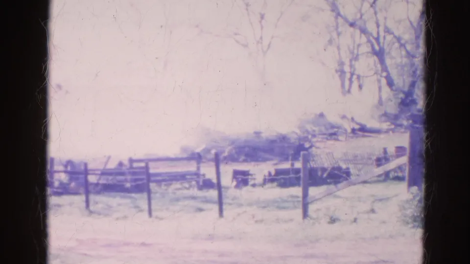 1968 Wauconda, Illinois home-movie frame showing lingering smoke behind a wooden fence and bare winter trees.