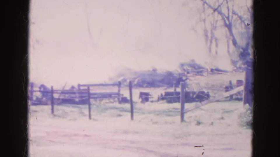 Late-1960s home-movie frame of smoke over a rural Wauconda fence line, with visible film wear and purple color fading.