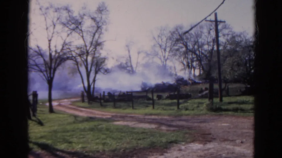1968 Wauconda, Illinois rural view with smoke behind fencing, a curving dirt track, bare trees, utility poles, and open grass.