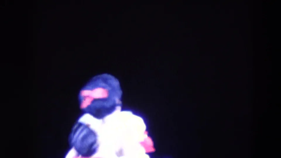 In 1969 Chicago home-movie footage, two ice skaters appear under strong blue-purple lighting on a dark rink.
