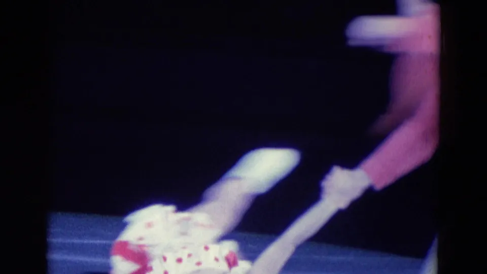 A white-costumed skater appears extended beside a partner in pink under theatrical rink lighting in the 1969 Chicago clip.