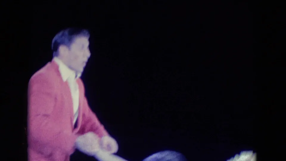 Chicago 1969 8mm frame showing a male ice performer in a pink jacket and white trousers against a dark rink.