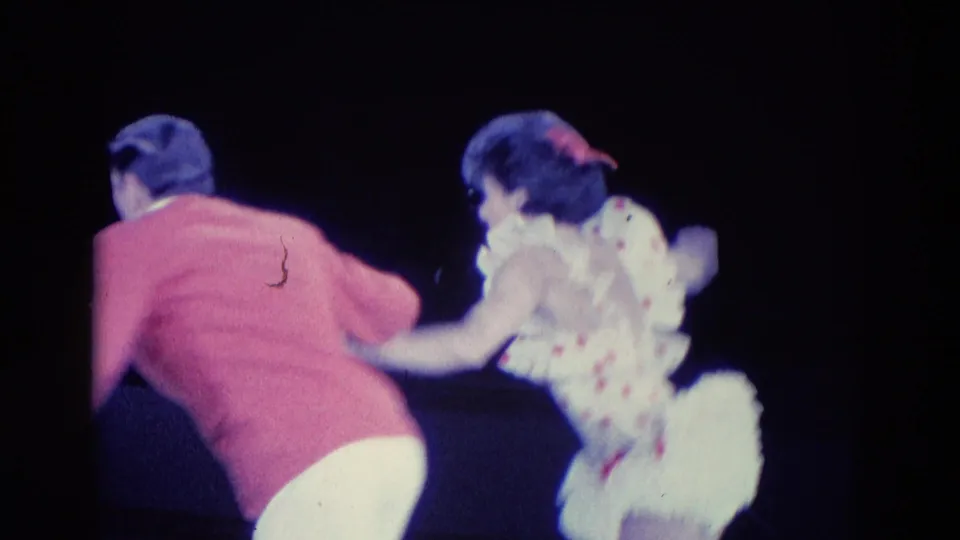 Chicago 1969 8mm frame showing paired ice dancers, including a woman in a polka-dot dress, turning near a cat-like figure.