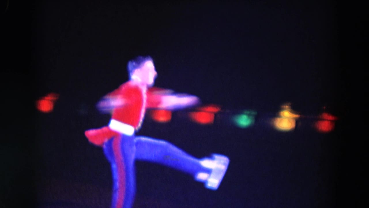 1969 Chicago skating-show frame with a red-and-blue costumed skater extending a leg during a fast glide on the ice.